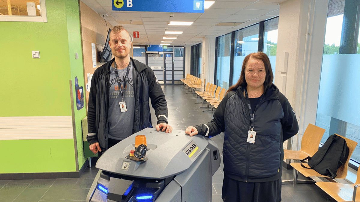 kaksi työnjohtajaa seisoo sairaalan käytävässä lattianpesurobotin vierellä