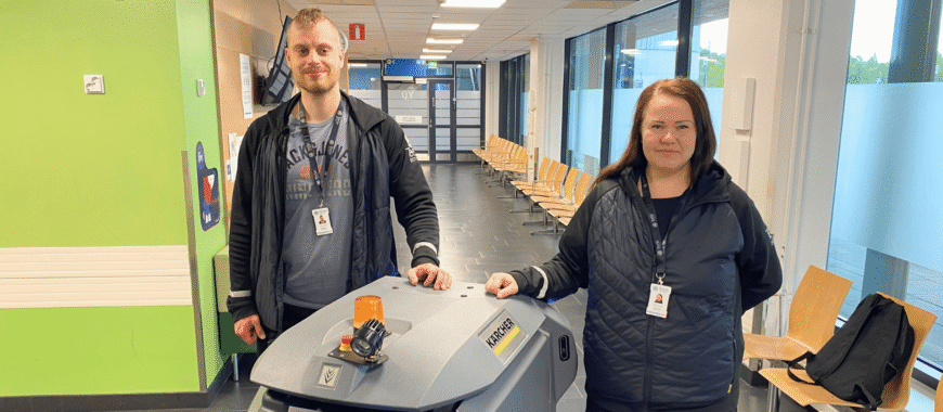 kaksi työnjohtajaa seisoo sairaalan käytävässä lattianpesurobotin vierellä